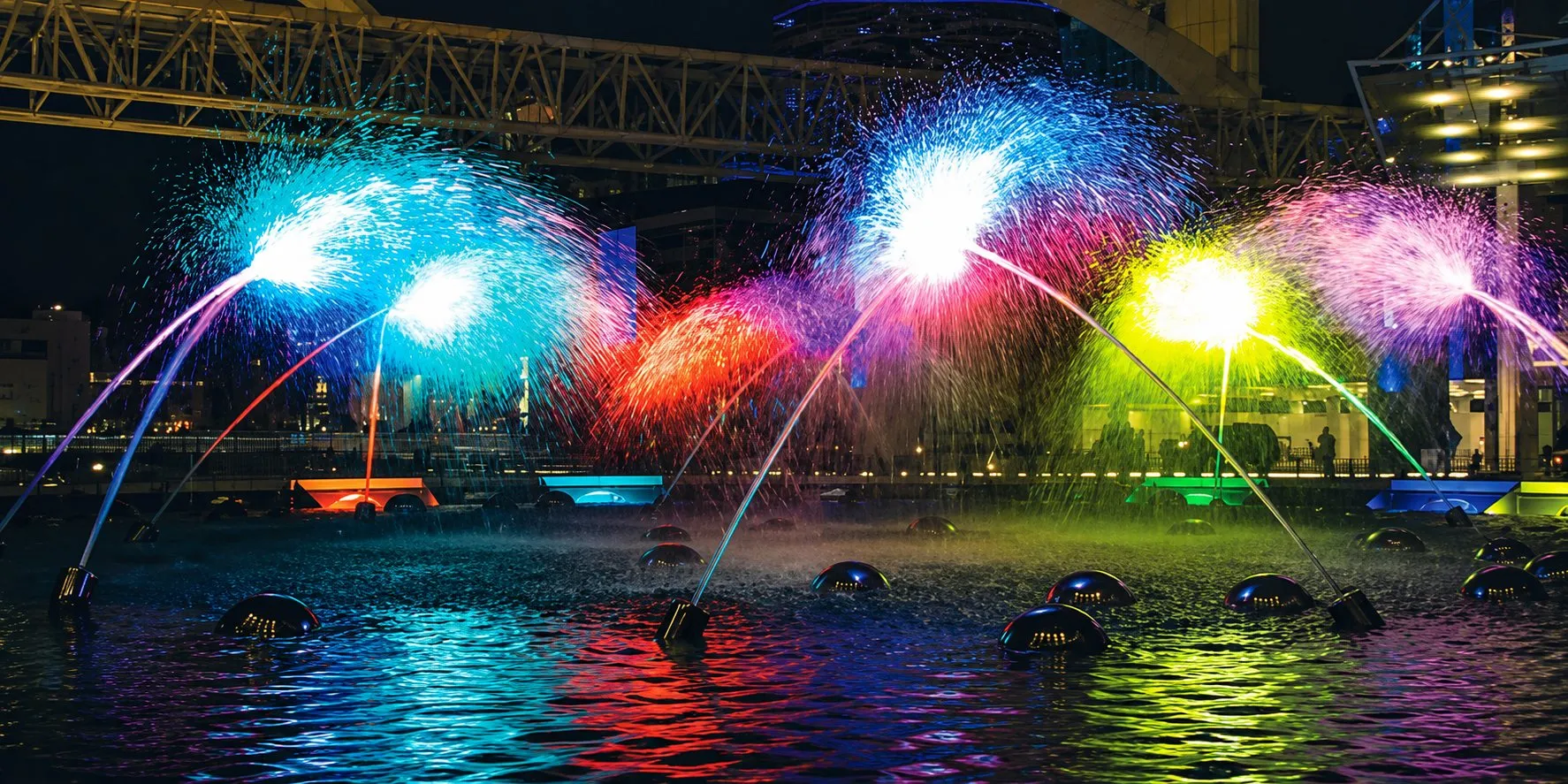 Illuminated arching jets in a choreographed fountain basin at night