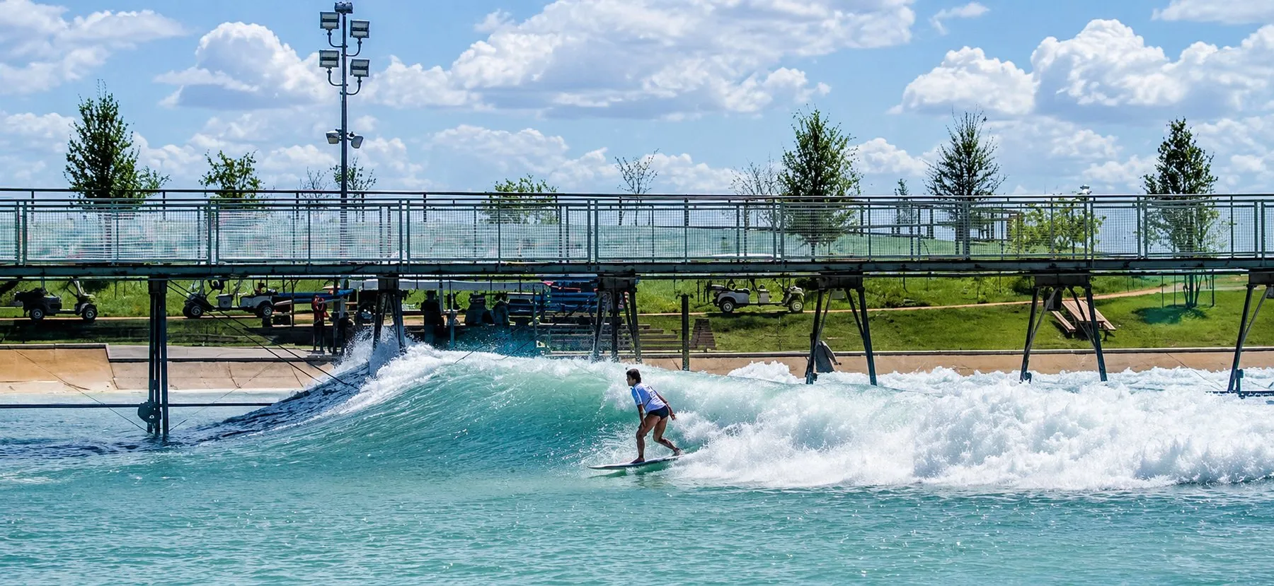 Surfer riding a machine-generated wave across a surf park lagoon