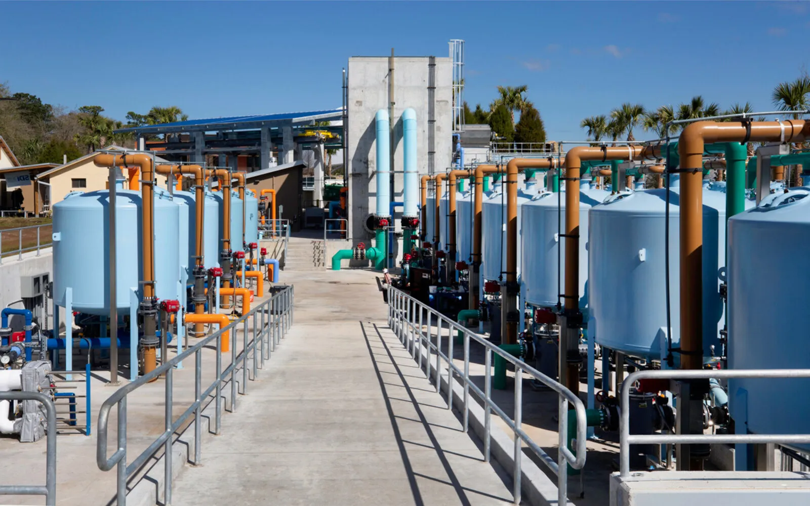 Rows of pressure sand filters with process piping and valve manifolds at an outdoor life support installation